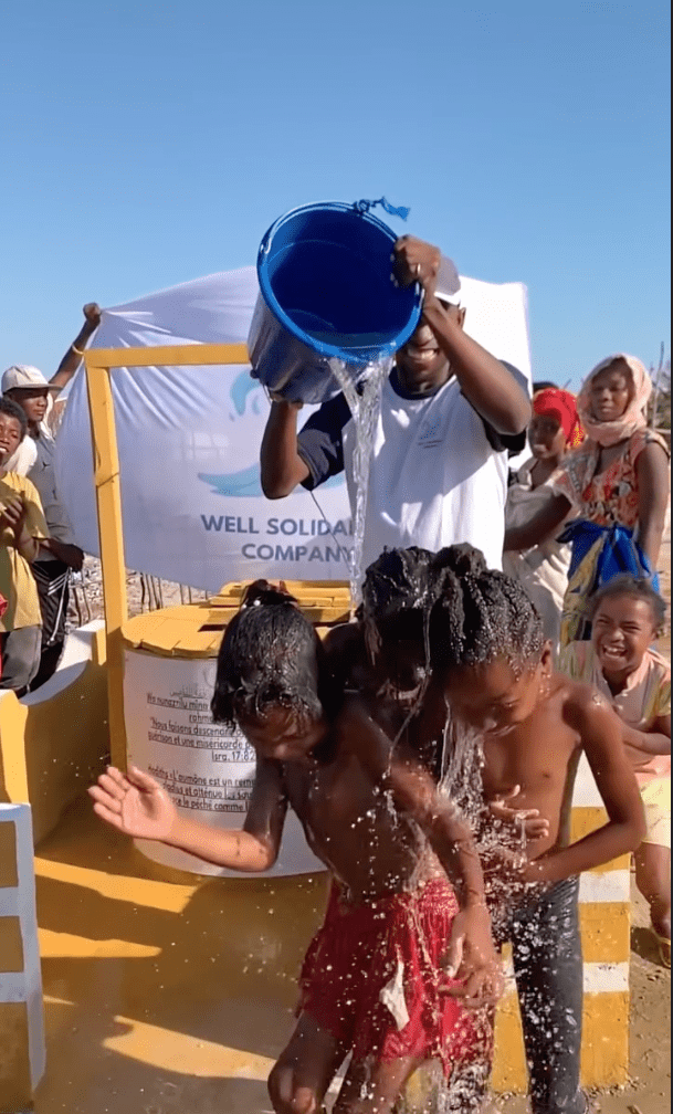 Enfants jouent sous l'eau d'un seau.